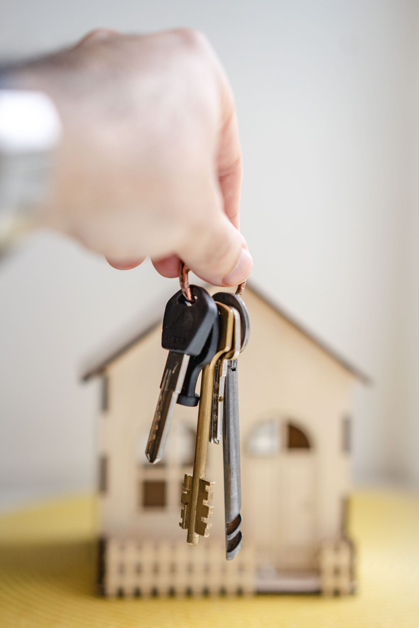 A hand holding keys in front of a model house representing selling a home.